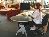 YAKETY YAK 202 Desk with its open and inviting form is positioned alongside an area where customers can sit and use devices.